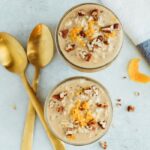 Top down of two jars of orange vanilla overnight oats, topped with orange zest and pecans, with two gold spoons.