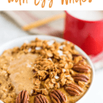 Bowl of protein pumpkin oatmeal with egg whites topped with granola, almond butter and pecans. Mug and spoon are to the side.