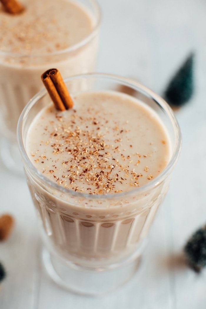 Eggnog in a glass with a cinnamon stick and topped with grated nutmeg.