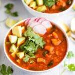 Two bowls of Mexican sweet potato chicken soup with avocado, radishes, and cilantro. Half an avocado, limes, and cilantro on the side.