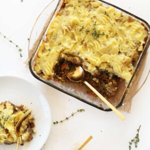 Vegan shepard's pie in a baking dish, with two servings removed. The servings are on plates next to the baking dish.