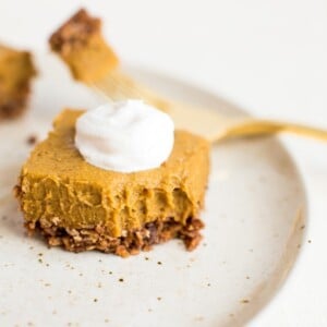 Pumpkin pie bar with a bite taken out of it on a white plate.