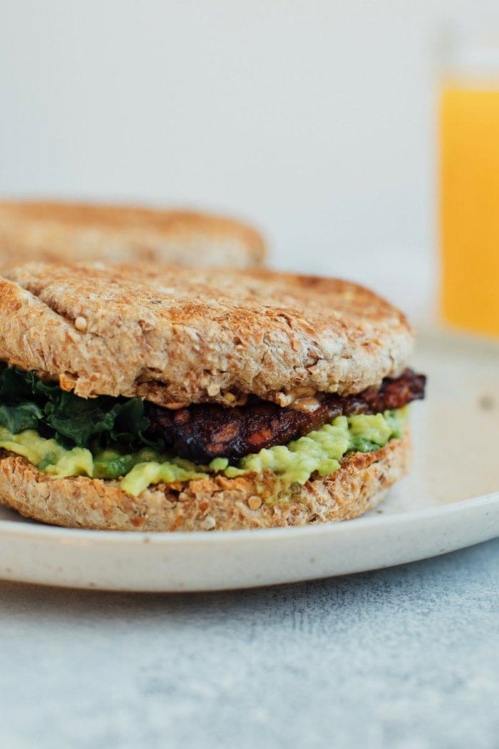 A vegan breakfast sandwich loaded with all the goods: creamy avocado, almond butter, sautรฉed kale and tempeh bacon, served on a perfectly toasted english muffin.