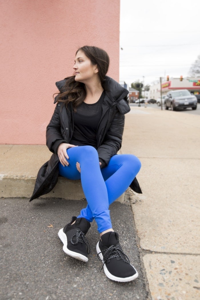 Woman in activewear and a jacket sitting on the sidewalk.
