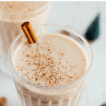 Glass of clean eating eggnog garnished with a stick of cinnamon and grated nutmeg. Text above reads "Clean Eating Dairy-Free Eggnog".