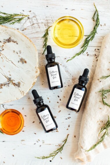 Overhead shot of 3 bottles of DIY facial oil on white tray and white wood table with dried lavender buds.