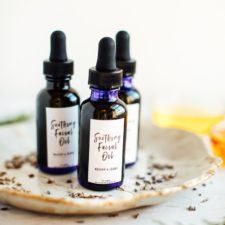 3 bottles of DIY facial oil on white wood table with dried lavender buds.
