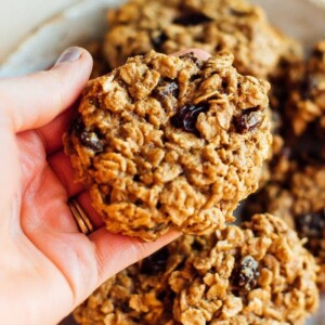 A woman holding a dairy-free chewy oatmeal cookies above a plate.
