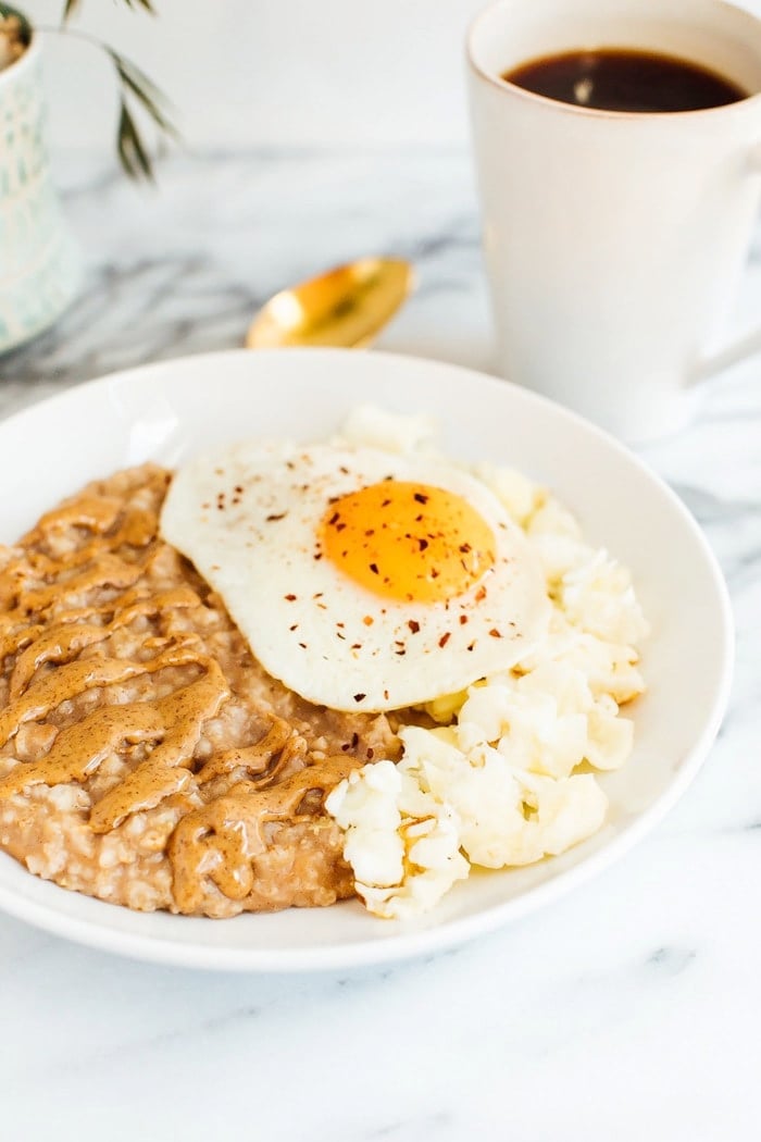 Sweet + Savory Egg and Oatmeal Combo Bowl in a white bowl served with gold spoon and cup of coffee.