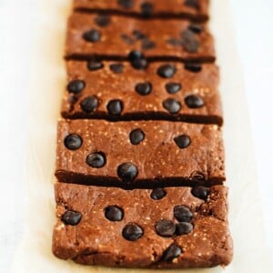 Peanut butter chocolate protein bars with chocolate chips in a row on a white textured surface.