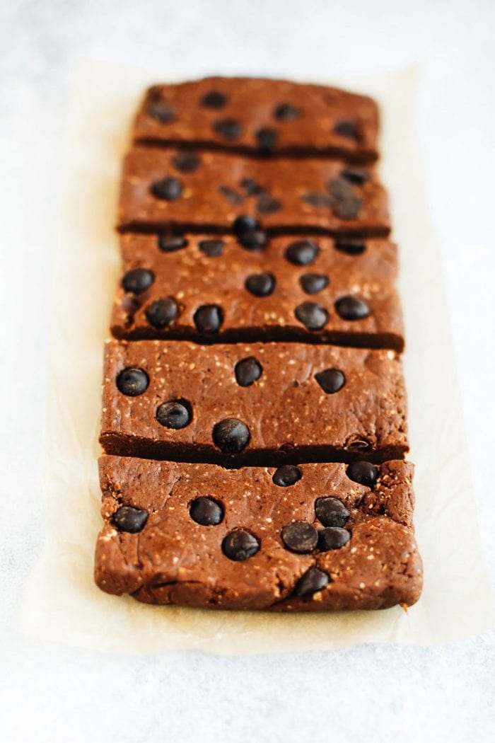 Peanut butter chocolate protein bars with chocolate chips in a row on a white textured surface.