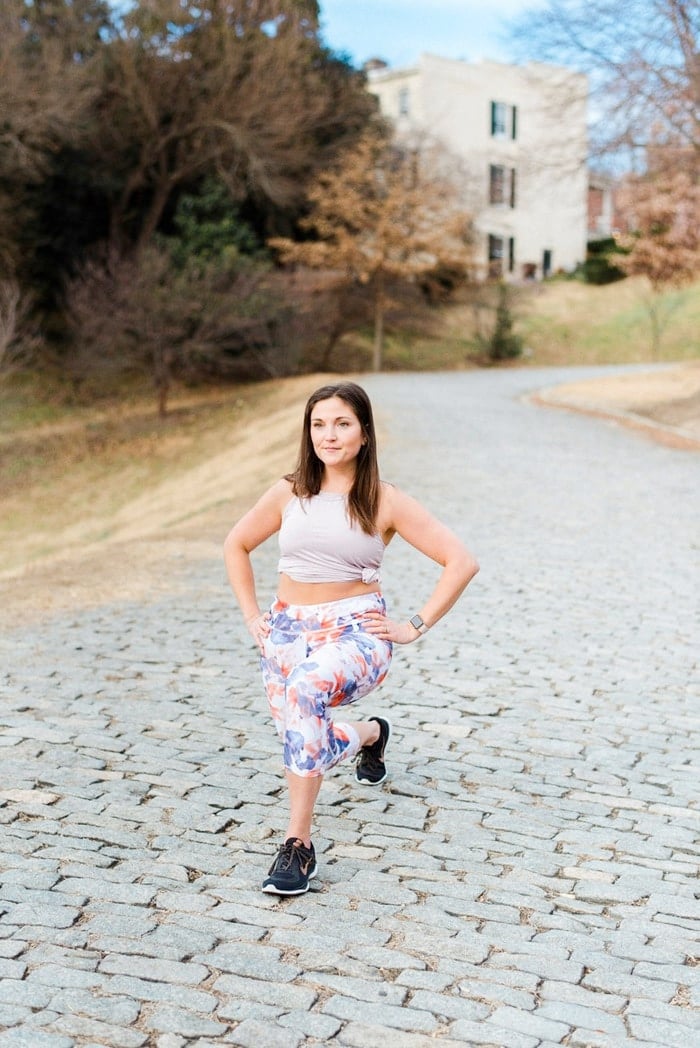 Woman lunging outside in floral athletic pants and sleeveless shirt.