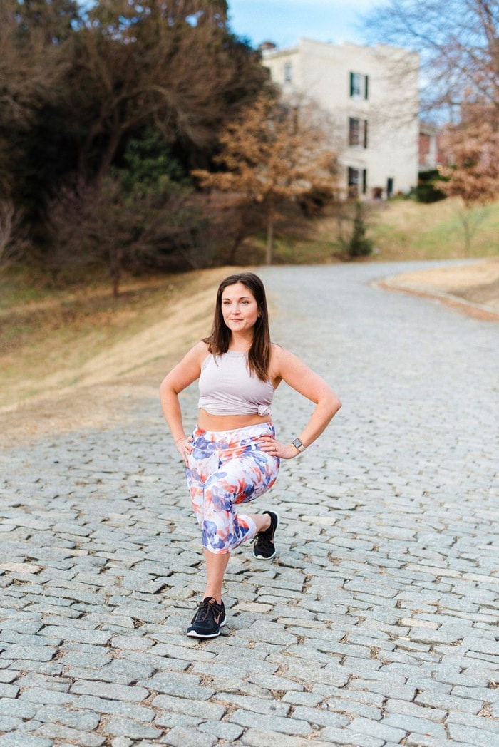 Woman lunging outside in floral athletic pants and sleeveless shirt.