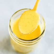 Turmeric tahini dressing in a jar with some on a spoon.