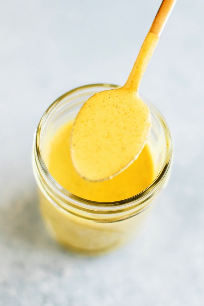 Golden Turmeric Tahini Dressing in a glass jar. Spoon, spooning some dressing.