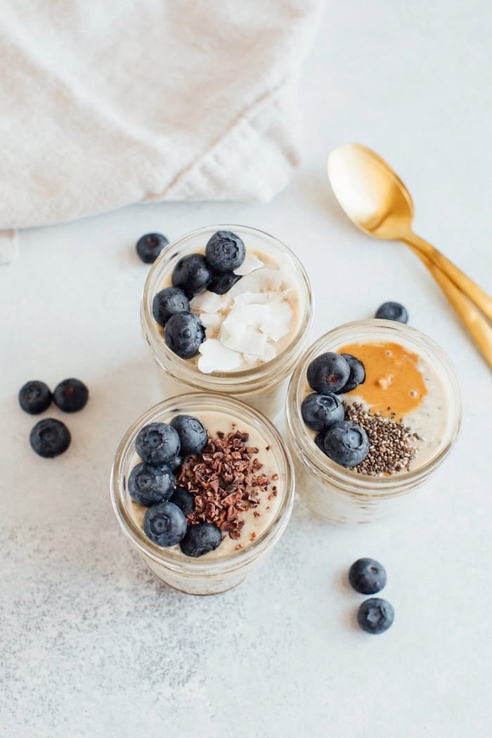 Three pint size mason jars with grain-free overnight "oats" topped with blueberries, cacao nibs, chia seeds and coconut. 