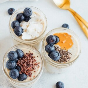 Three pint-size mason jars with grain-free overnight "oats" and toppings. Two gold spoons on the right.