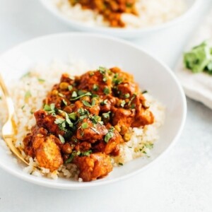 Tempeh tikka masala with chickpeas on cauliflower rice on a white plate.