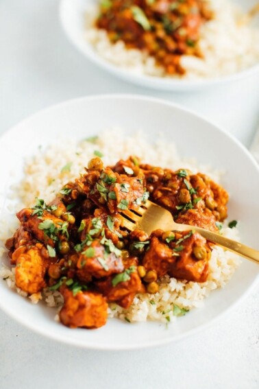 Tempeh tikka masala with chickpeas on cauliflower rice with a fork.