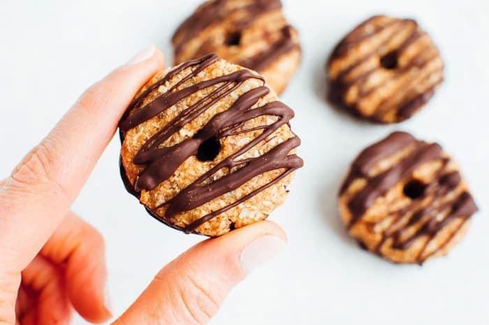 Hand holding one homemade Samoas cookie with three cookies in the background. 