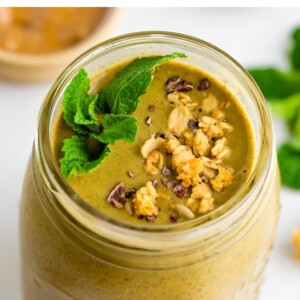 Mason jar with a mint chocolate chip smoothie garnished with cacao nibs, granola and mint.