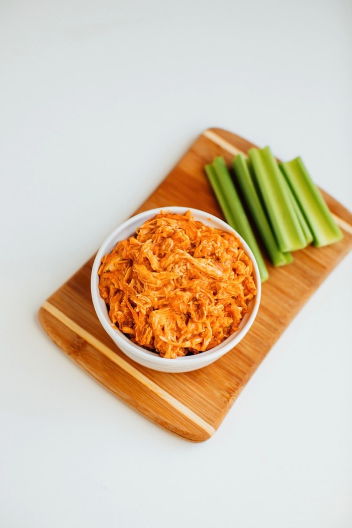 Slow cooker shredded buffalo chicken in a bowl with celery sticks on the side. 