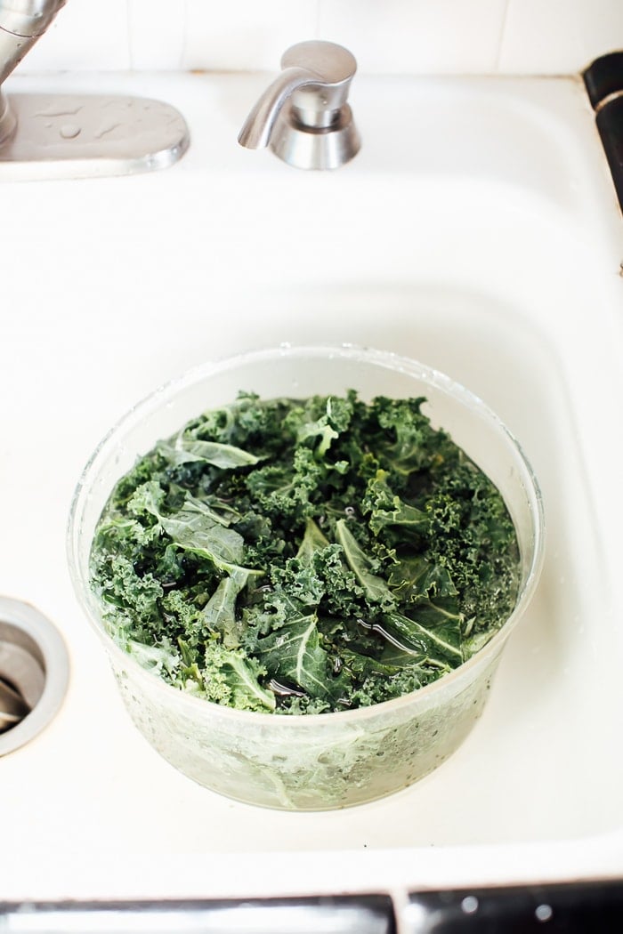 Salad spinner filled with water and kale in the sink. 