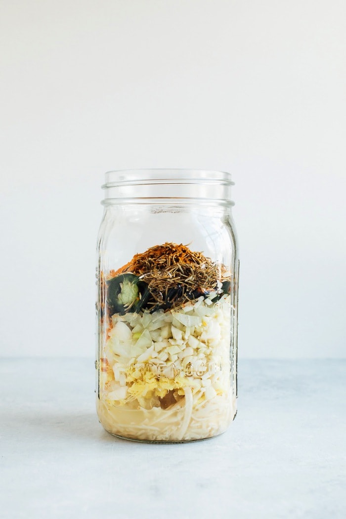 Adding all the roots, herbs and fresh vegetables into a mason jar for fire cider. Adding all the roots, herbs and fresh vegetables into a mason jar for fire cider.