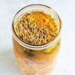 Adding all the roots, herbs and fresh vegetables into a mason jar for fire cider.