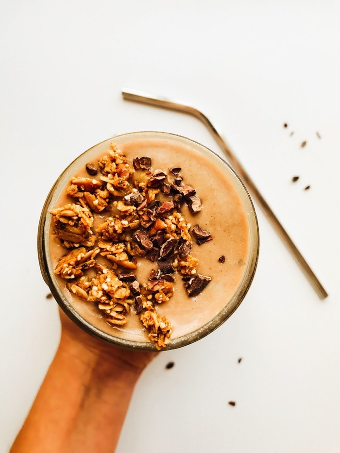 Overhead shot of a chocolate mint chip smoothie with granola in a mason jar with a stainless steel straw on the surface next to it. 