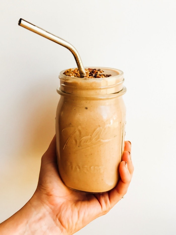 Chocolate mint chip smoothie in a mason jar with a stainless steel straw, being held by a women's hand. 