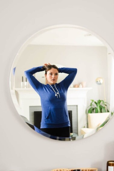 Woman getting ready for a run, pulling hair into a ponytail in the living room.