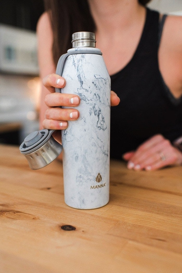 Close up of a woman holding a water bottle at a table.