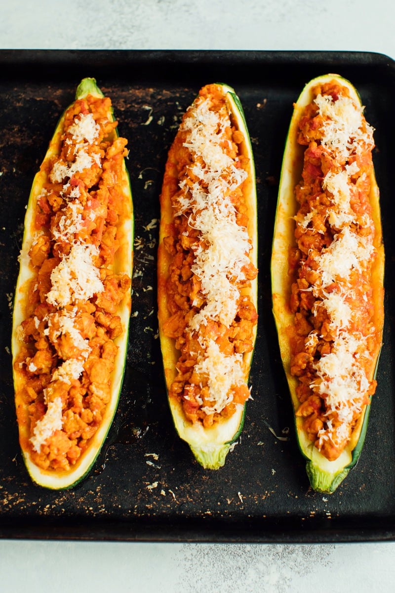 Three zucchini boats on a baking stone with turkey and parmesan on top. 