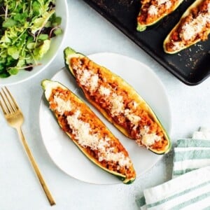 Two healthy zucchini boats on a plate with a baking stone and salad.