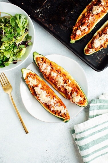 Two healthy zucchini boats on a plate with a baking stone and salad.