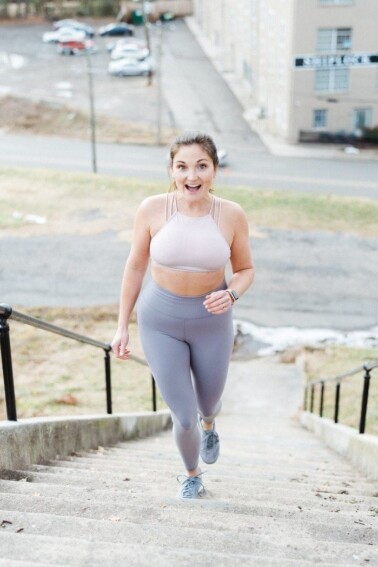 Photo of woman in workout gear, smiling and walking up steps in a park.