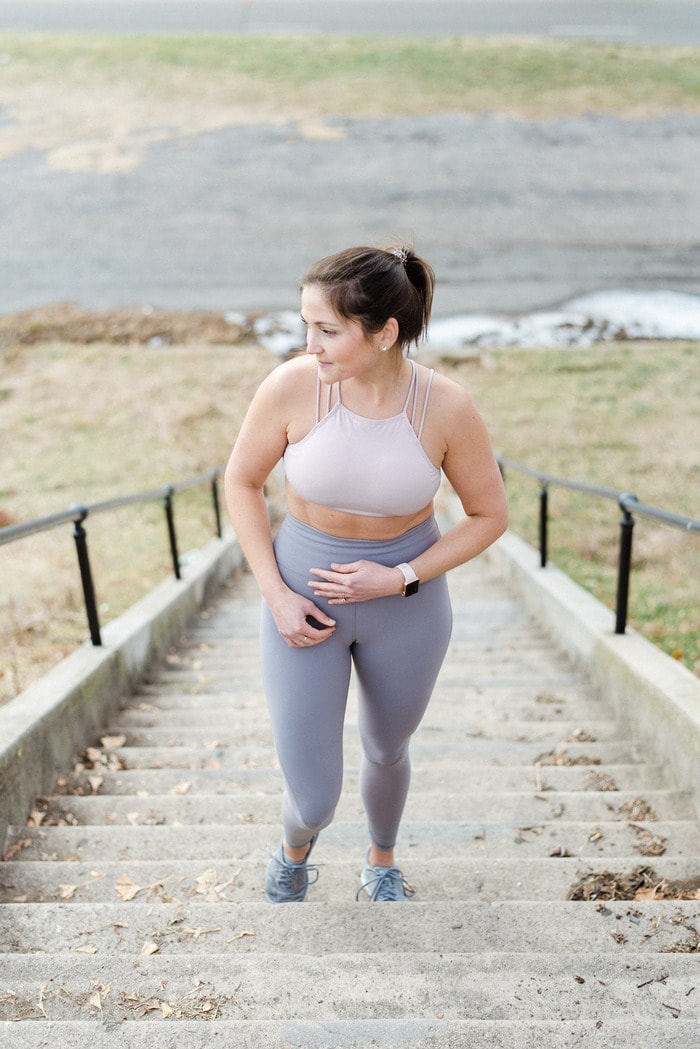 Photo of woman in workout gear walking up steps in a park with hand over belly. 
