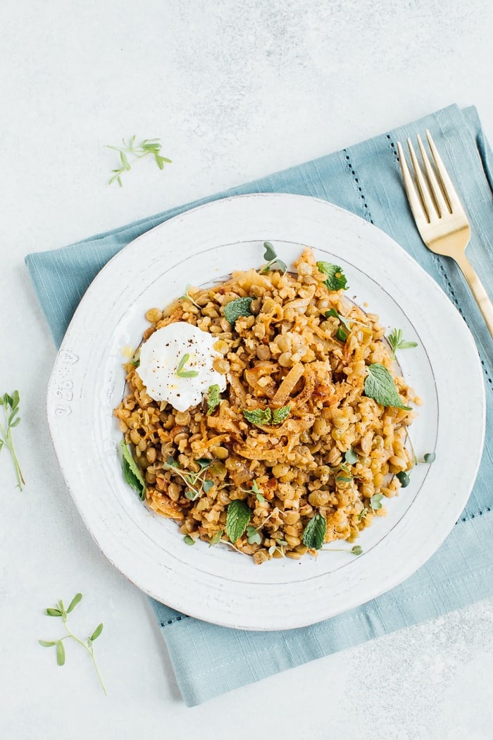 Caramelized onions, lentils and cauliflower rice on a rustic plate with a gold fork in the background. 