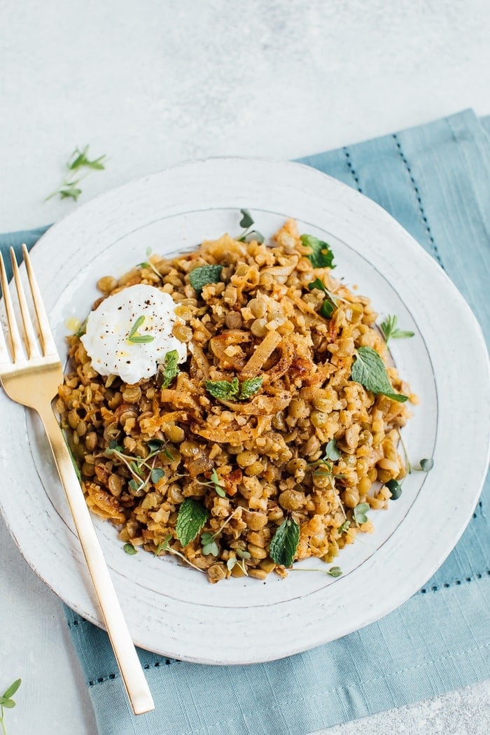 Caramelized onions, lentils and cauliflower rice on a rustic plate with a gold fork. 