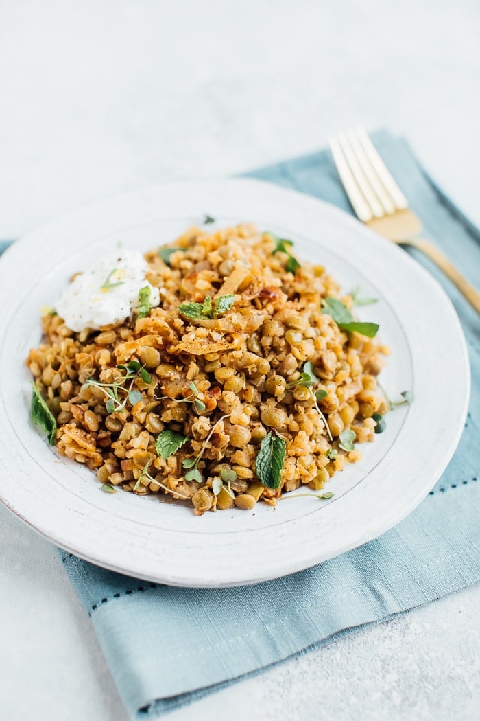 Caramelized onions, lentils and cauliflower rice on a rustic plate with a gold fork in the background. 