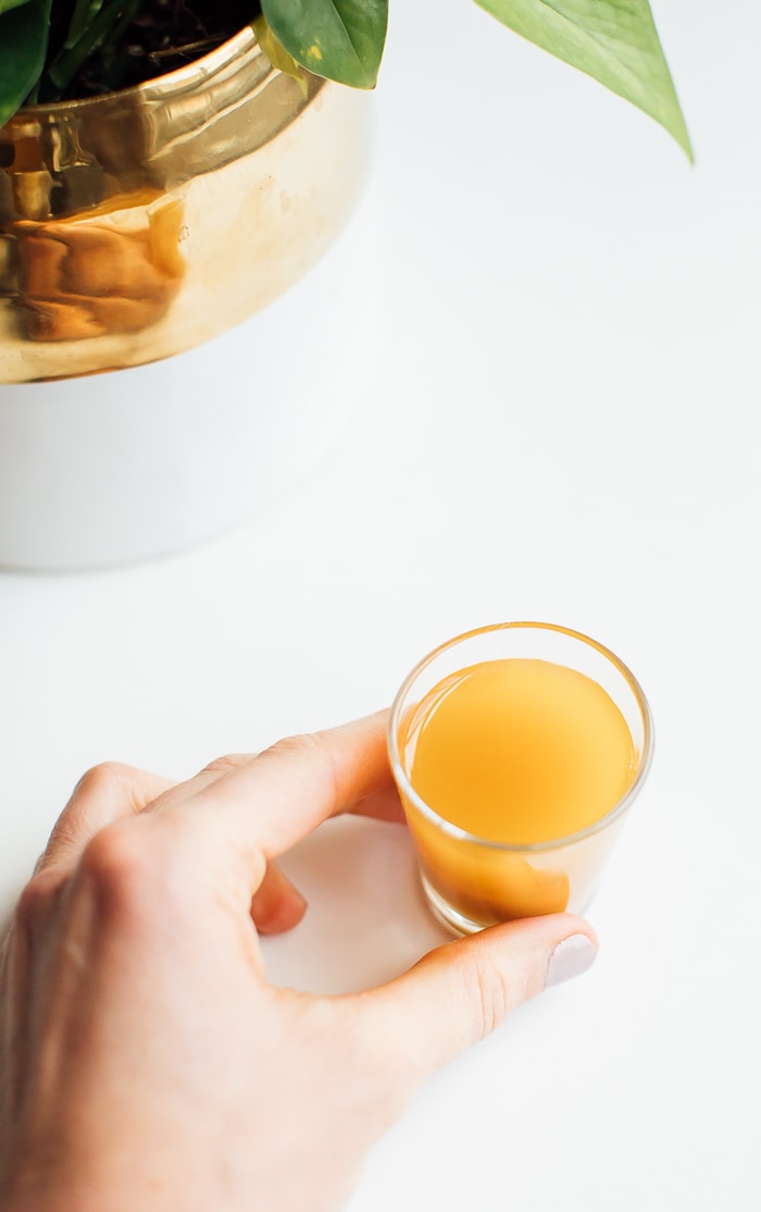 Fire cider in a shot glass being held by a woman's hand. 