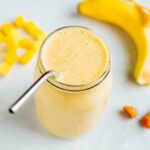 Golden milk smoothie surrounded by mango chunks, banana, and ginger.