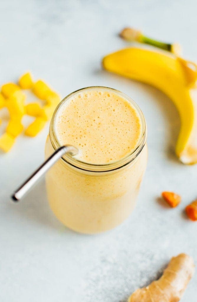 Golden milk smoothie surrounded by mango chunks, banana, and ginger.