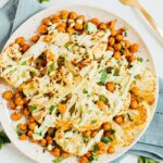 Top down toasted cauliflower steaks with garbanzo beans on a plate with fork and blue napkin.