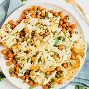 Top down toasted cauliflower steaks with garbanzo beans on a plate with fork and blue napkin.