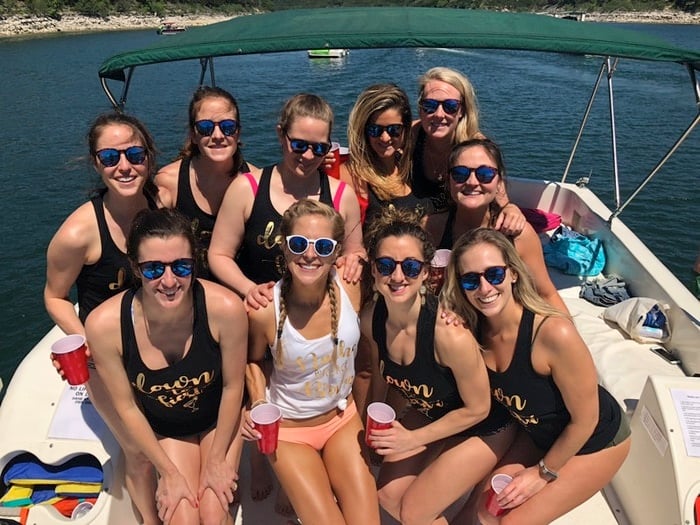 10 women smiling while on a boat, wearing matching tank tops.