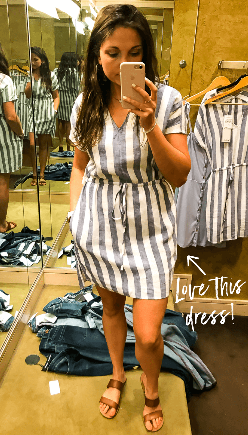 Photo of woman wearing a blue-grey and white striped cotton dress in a dressing room. White texts reads "love this dress!" with an arrow pointing to the dress.
