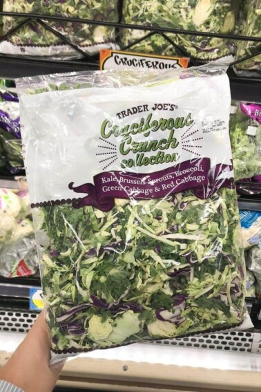 A hand holding a bag of Trader Joe's mixed greens.