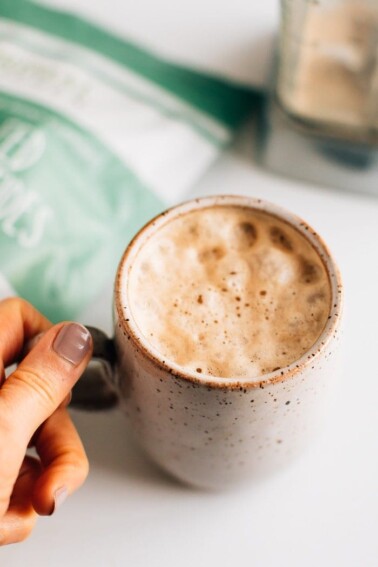 Hand holding a mug next to a bag of collagen.